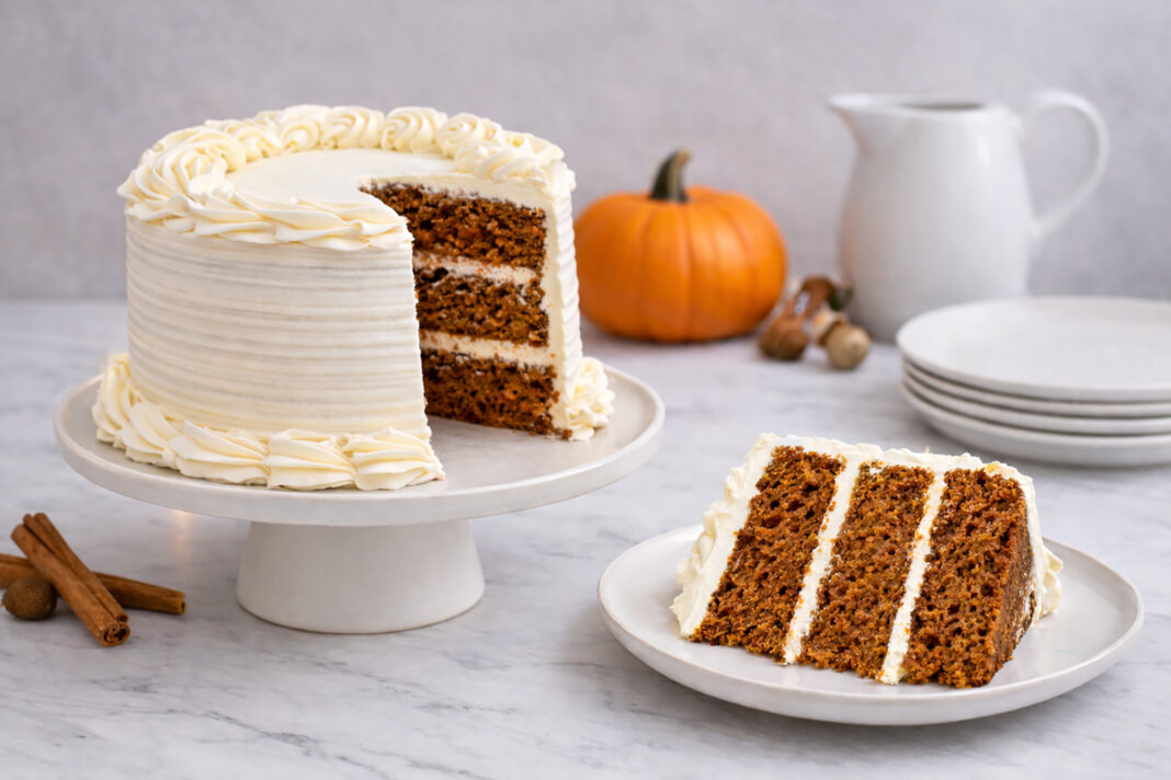 Pumpkin spice layer cake with cream cheese frosting, shown with a slice removed and served on a plate.