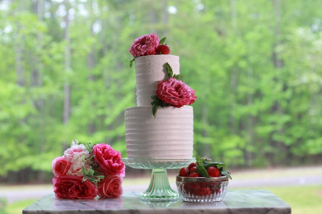 Two-tier strawberry cake with pale pink frosting, decorated with fresh strawberries and pink roses.
