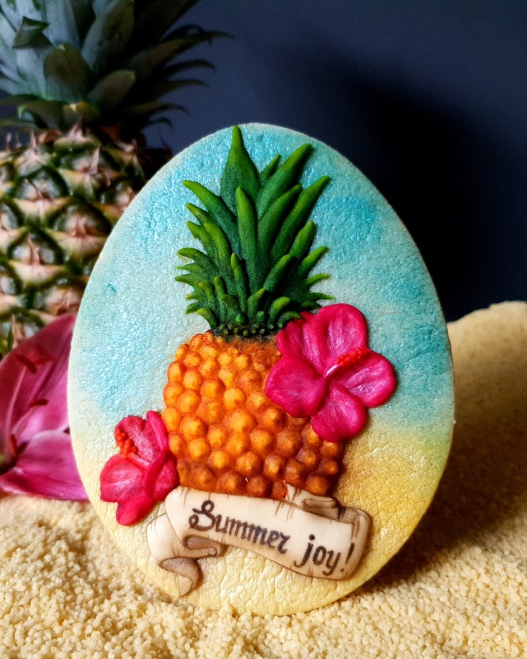Pineapple-themed decorated cookie with bright hibiscus flowers and a “Summer joy!” banner, displayed on a sandy tropical background.