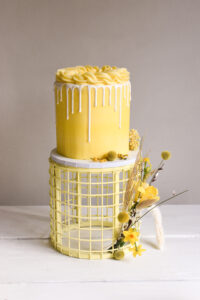 A yellow cake sits on a matching yellow cake stand.